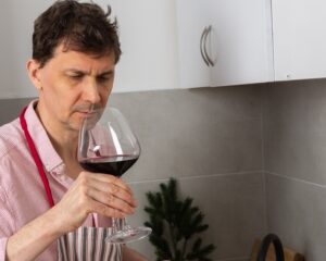 man is in a kitchen preparing a pre-Christmas dinner. He is focused on baking chicken with potatoes while serving himself a glass of red wine
